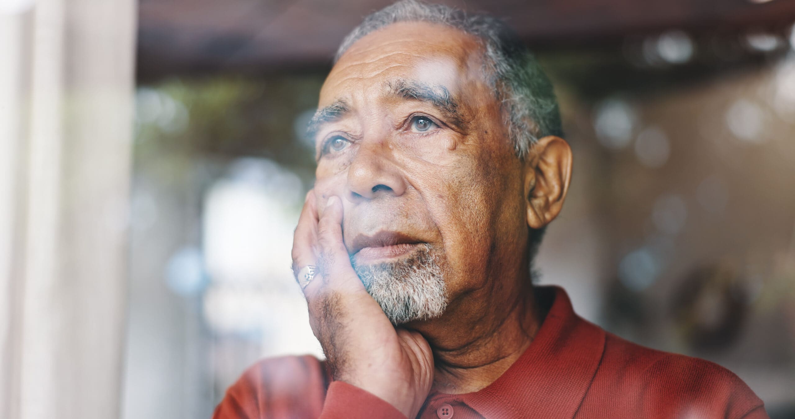 Depression, window and thinking with senior man in retirement home for loss, memories or nostalgia. Lonely, regret and sadness with unhappy person in apartment for anxiety, dementia or stress