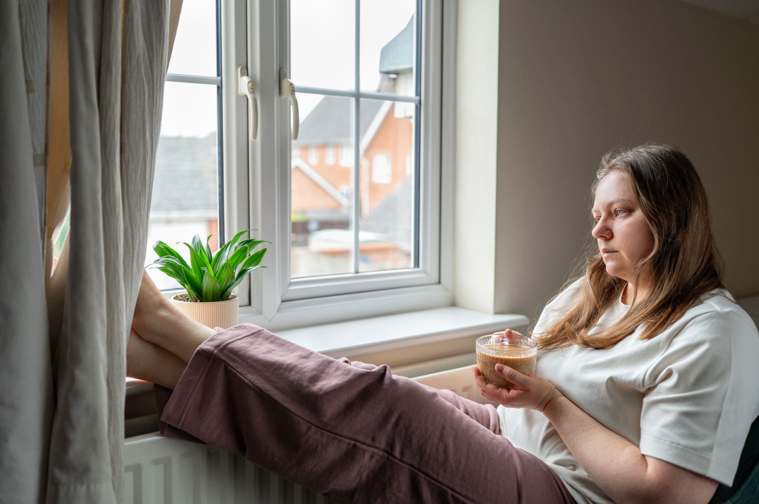 Exhausted woman sitting by window with coffee at home